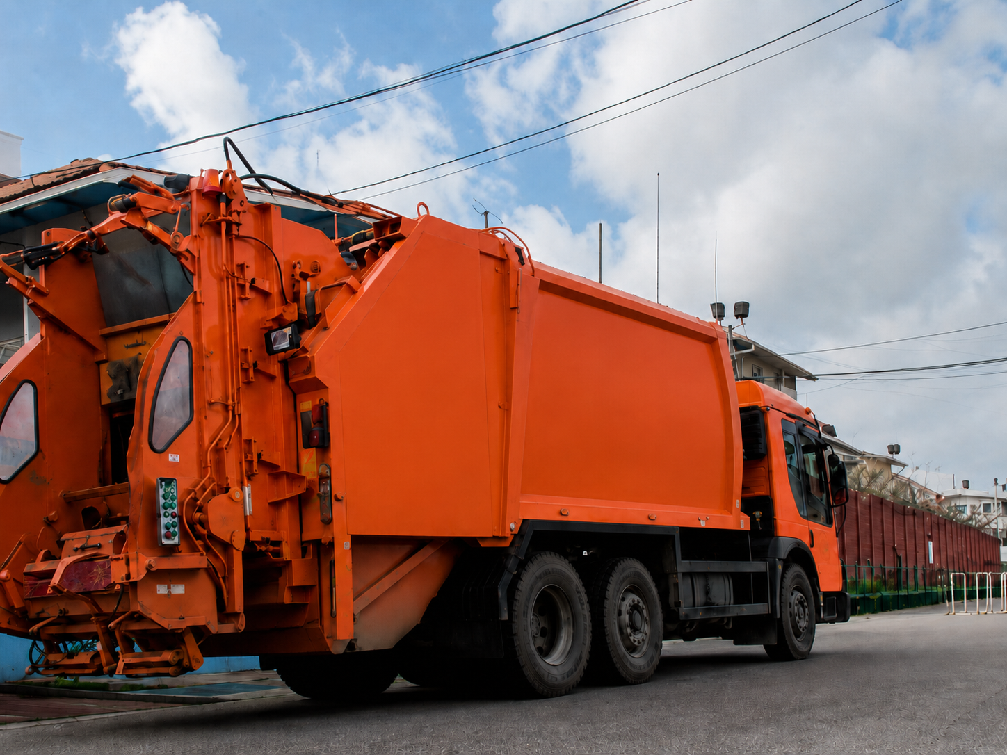 CEVONS orange rear-loader garbage collection truck on a Guyana residential street