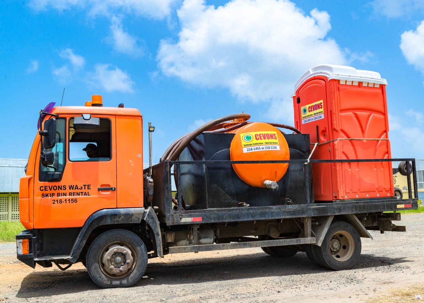 CEVONS service truck transporting a sealed vacuum tank and red portable toilet unit