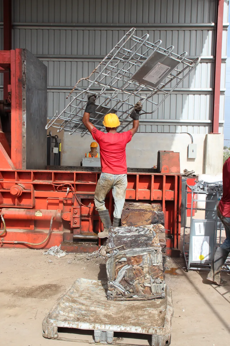 A CEVONS worker loading scrap steel into the baling press at the CEVONS recycling facility