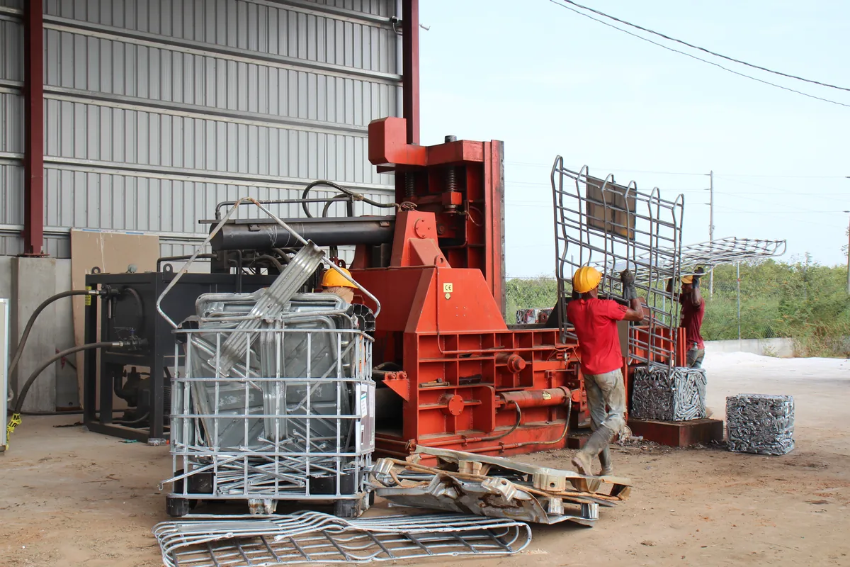 CEVONS crew feeding scrap metal into the baler beside stacked IBC cages at the recycling yard